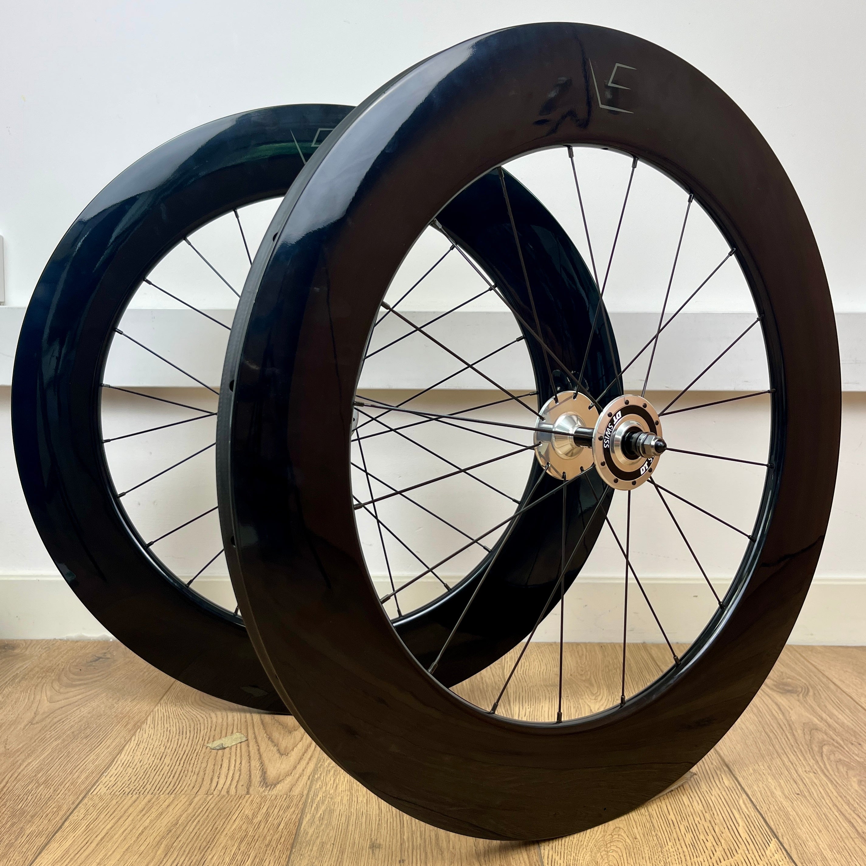 Two black bicycle wheels on a wooden floor with a white wall background