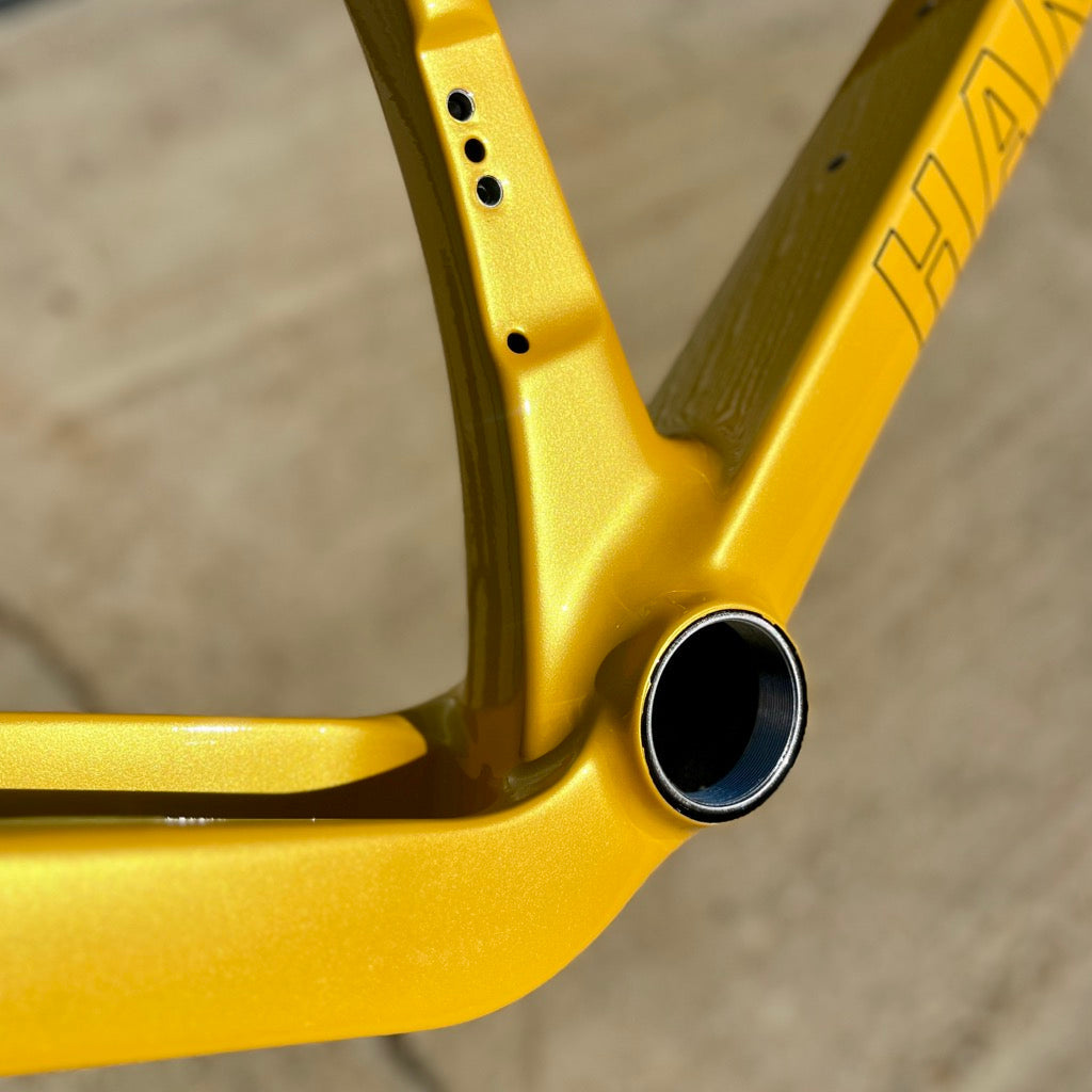 Close-up of a bright yellow bicycle frame showing the seat tube junction, seat post dropouts, and part of the down tube with the brand name Handsling visible.